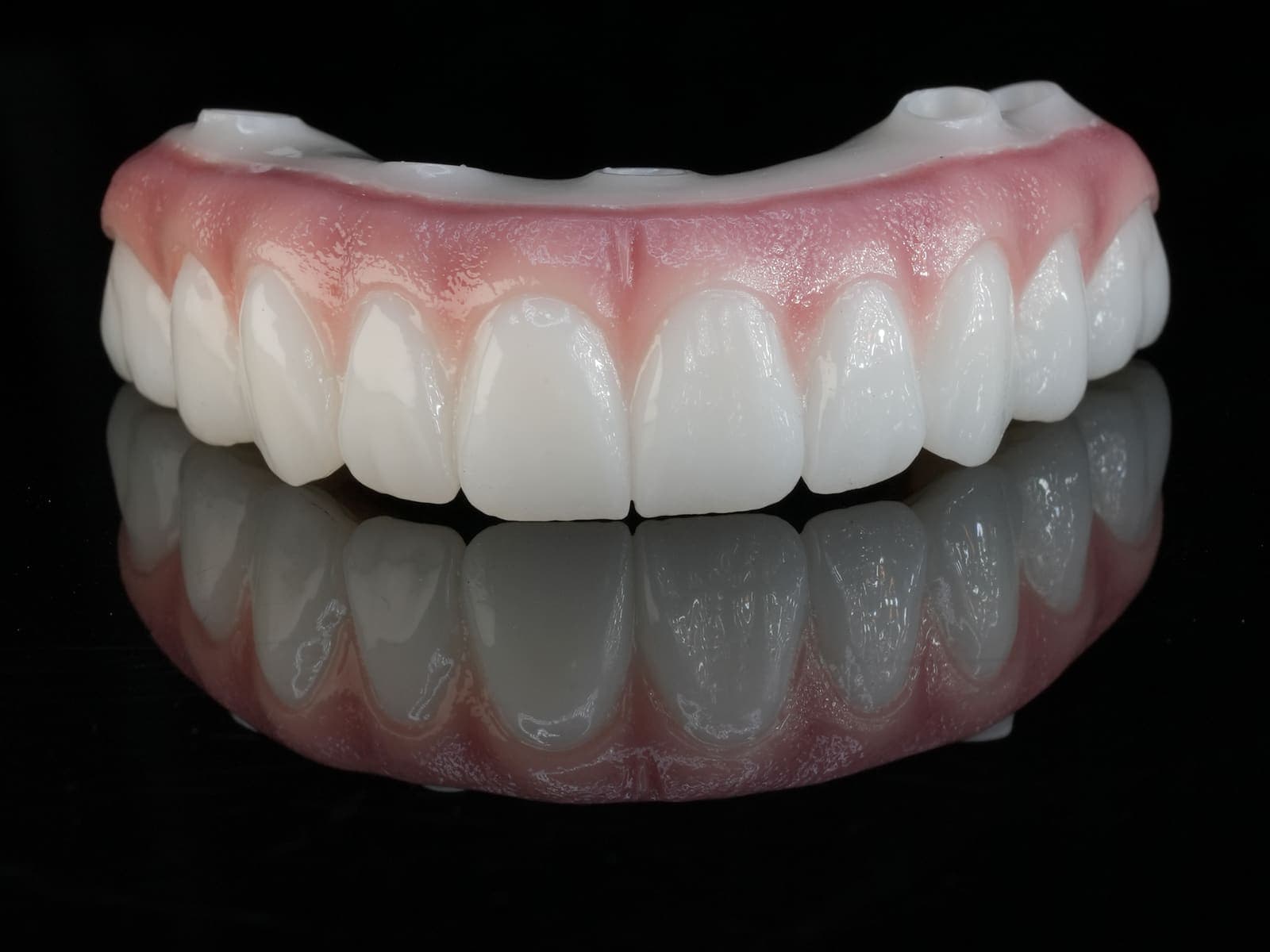 A finished upper All-on-X prosthesis, photographed from the front on black